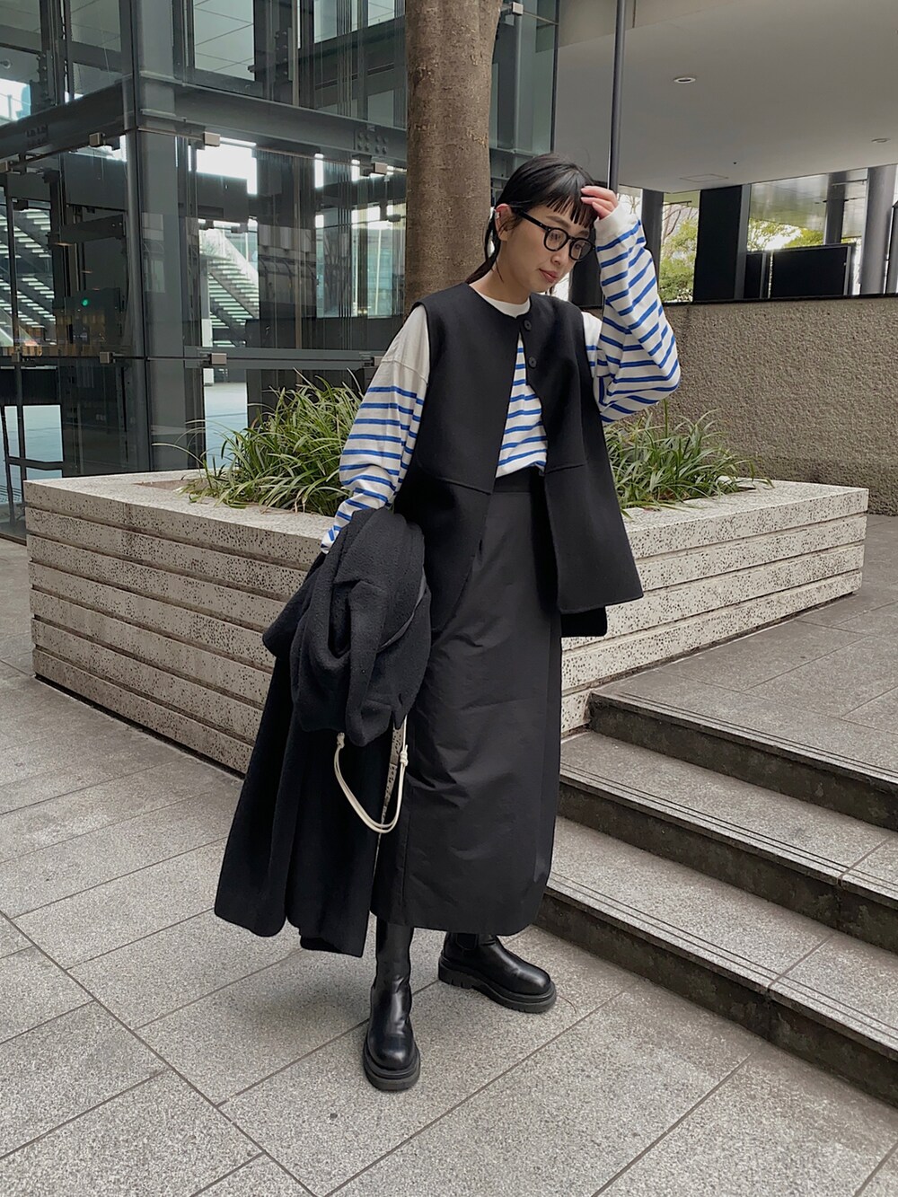 ブルー系のTシャツ/カットソー、ブラック系のチェスターコート、ブラック系のメガネを着用したレディースの冬コーディネートの2枚目の写真