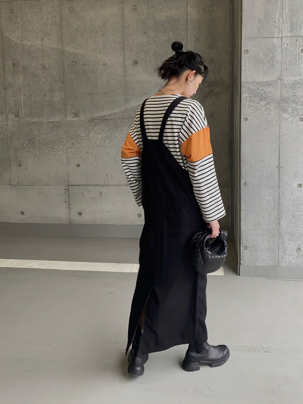ブラック系のブーツ、オレンジ系のTシャツ/カットソー、ブラック系のジャンパースカートを着用したレディースの春コーディネートの4枚目の写真