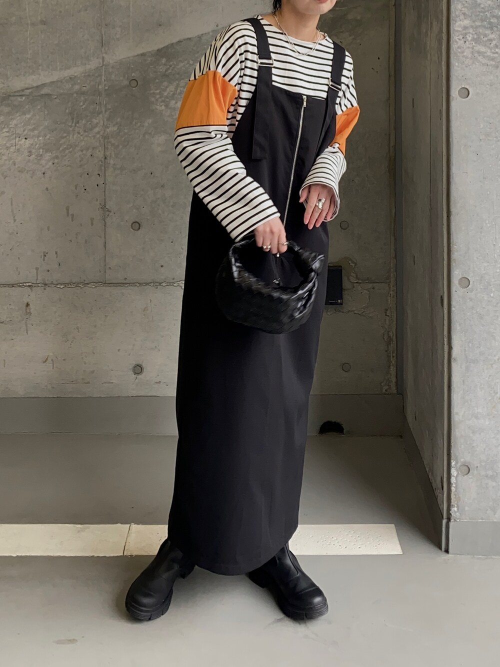 ブラック系のブーツ、オレンジ系のTシャツ/カットソー、ブラック系のジャンパースカートを着用したレディースの春コーディネートの2枚目の写真