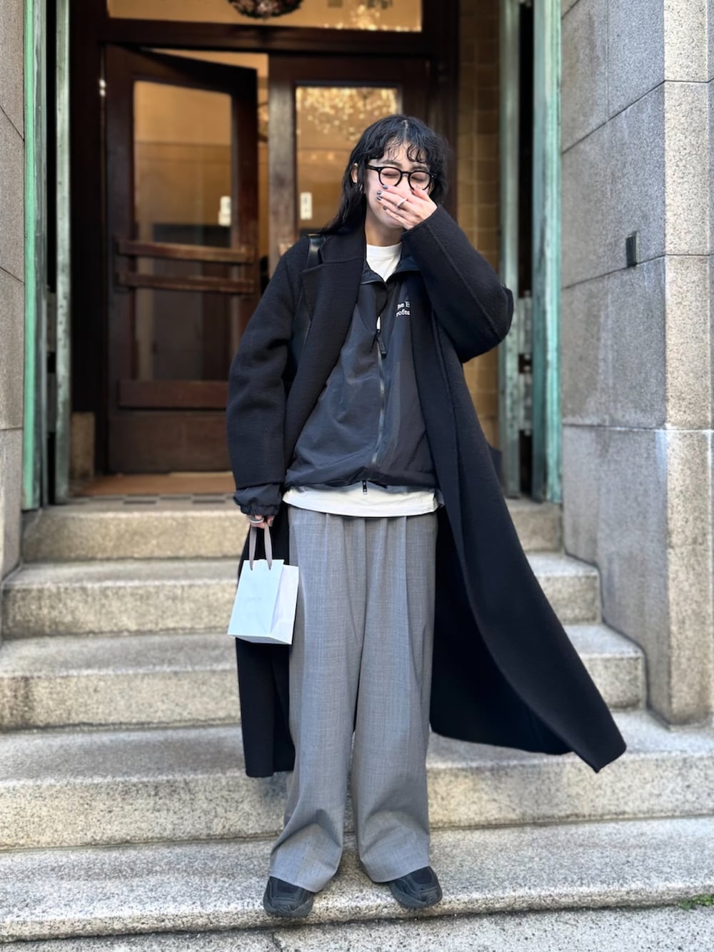 ブラック系のチェスターコート、ブラック系のナイロンジャケット、グレー系のスラックスを着用したレディースの冬コーディネートの2枚目の写真