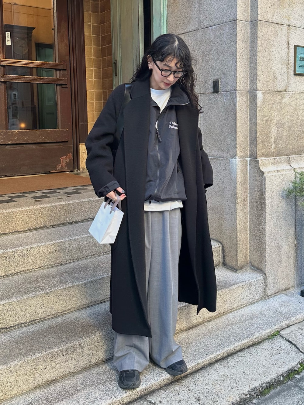 ブラック系のチェスターコート、ブラック系のナイロンジャケット、グレー系のスラックスを着用したレディースの冬コーディネートの5枚目の写真