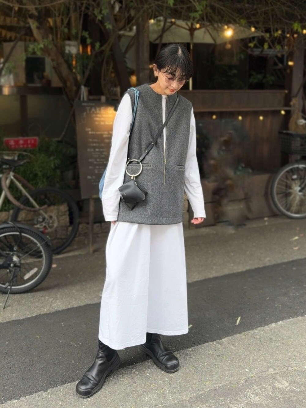 グレー系のベスト、ブラック系のショルダーバッグ、ブラック系のブーツを着用したレディースの秋コーディネートの3枚目の写真