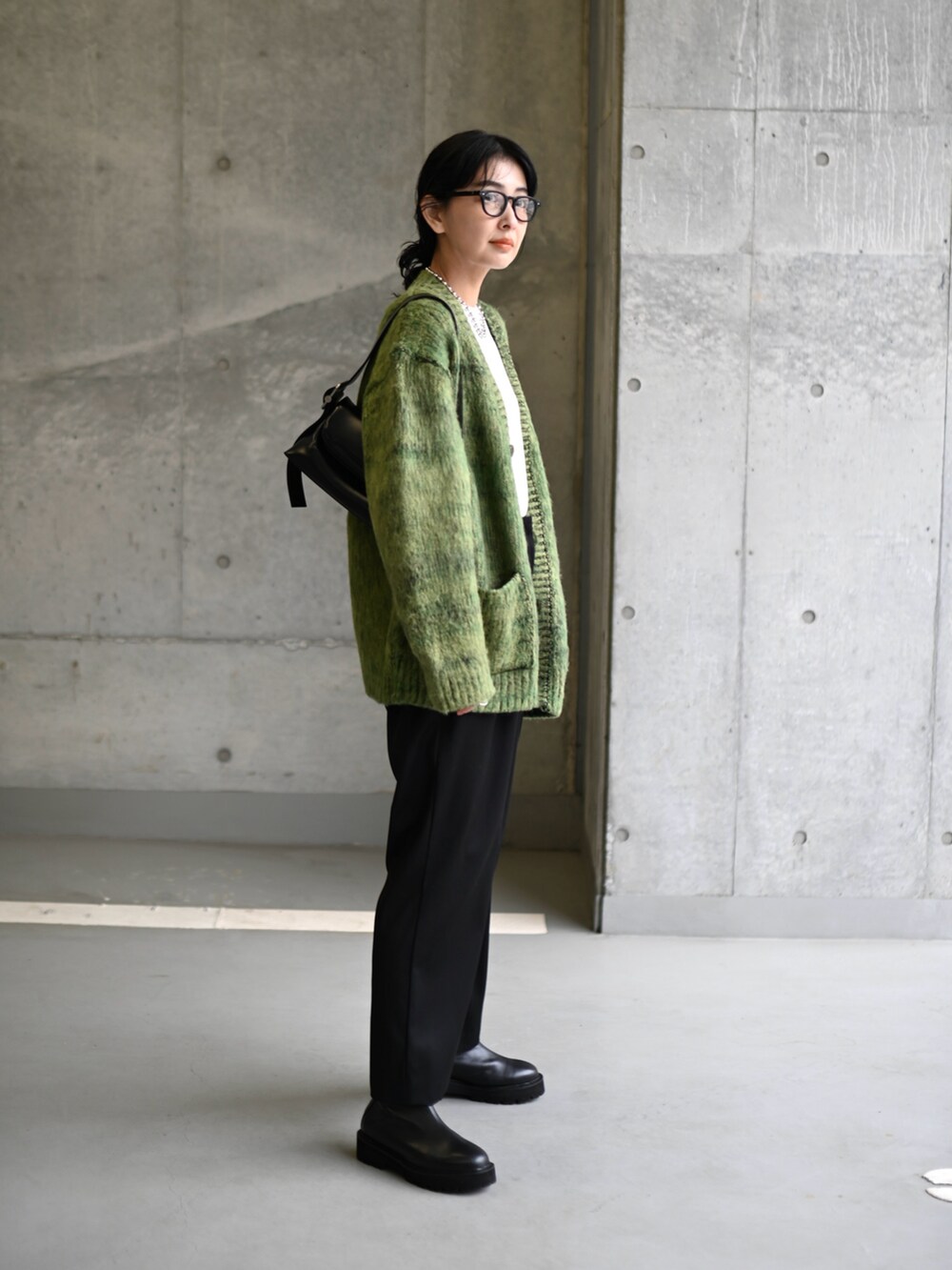 グリーン系のニット/セーター、ブラック系のスラックス、ブラック系のブーツを着用したレディースの冬コーディネートの2枚目の写真