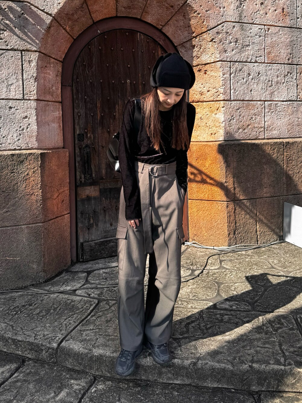 グレー系のパンツ、ブラック系のスニーカー、ブラック系のショルダーバッグを着用したレディースの秋コーディネートの2枚目の写真