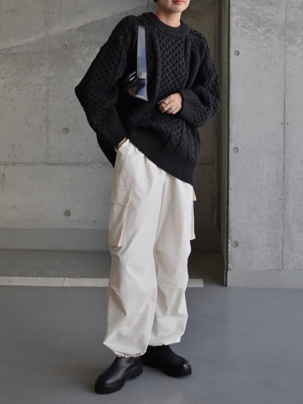 ブラック系のニット/セーター、ブラック系のショルダーバッグ、ブラック系のブーツを着用したレディースの秋コーディネートの4枚目の写真