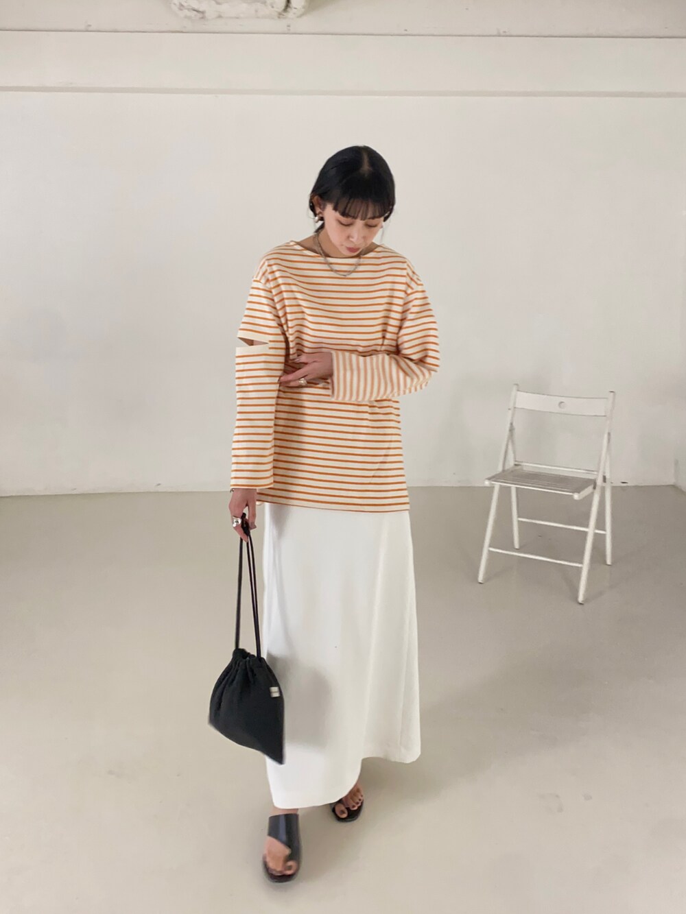 オレンジ系のTシャツ/カットソー、ホワイト系のスカート、ブラック系のショルダーバッグを着用したレディースの春コーディネートの3枚目の写真