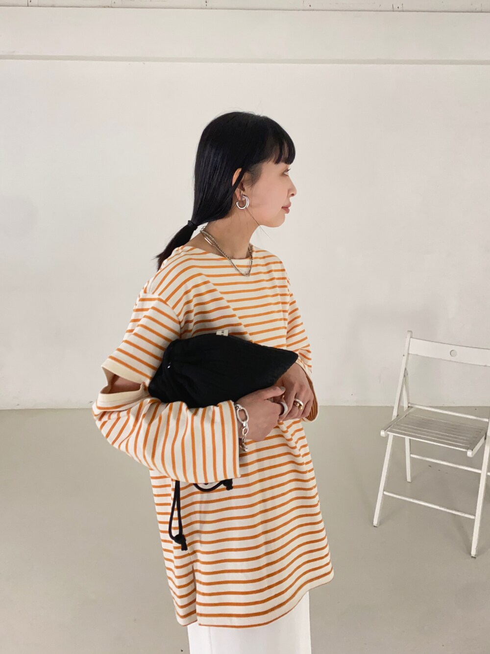 オレンジ系のTシャツ/カットソー、ホワイト系のスカート、ブラック系のショルダーバッグを着用したレディースの春コーディネートの2枚目の写真