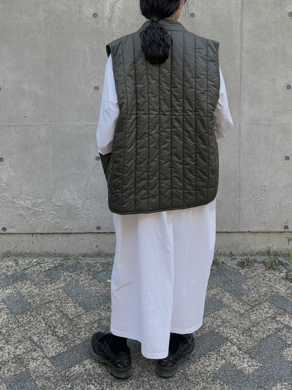 グリーン系のベスト、ブラック系のスニーカー、ブラック系のショルダーバッグを着用したレディースの秋コーディネートの3枚目の写真