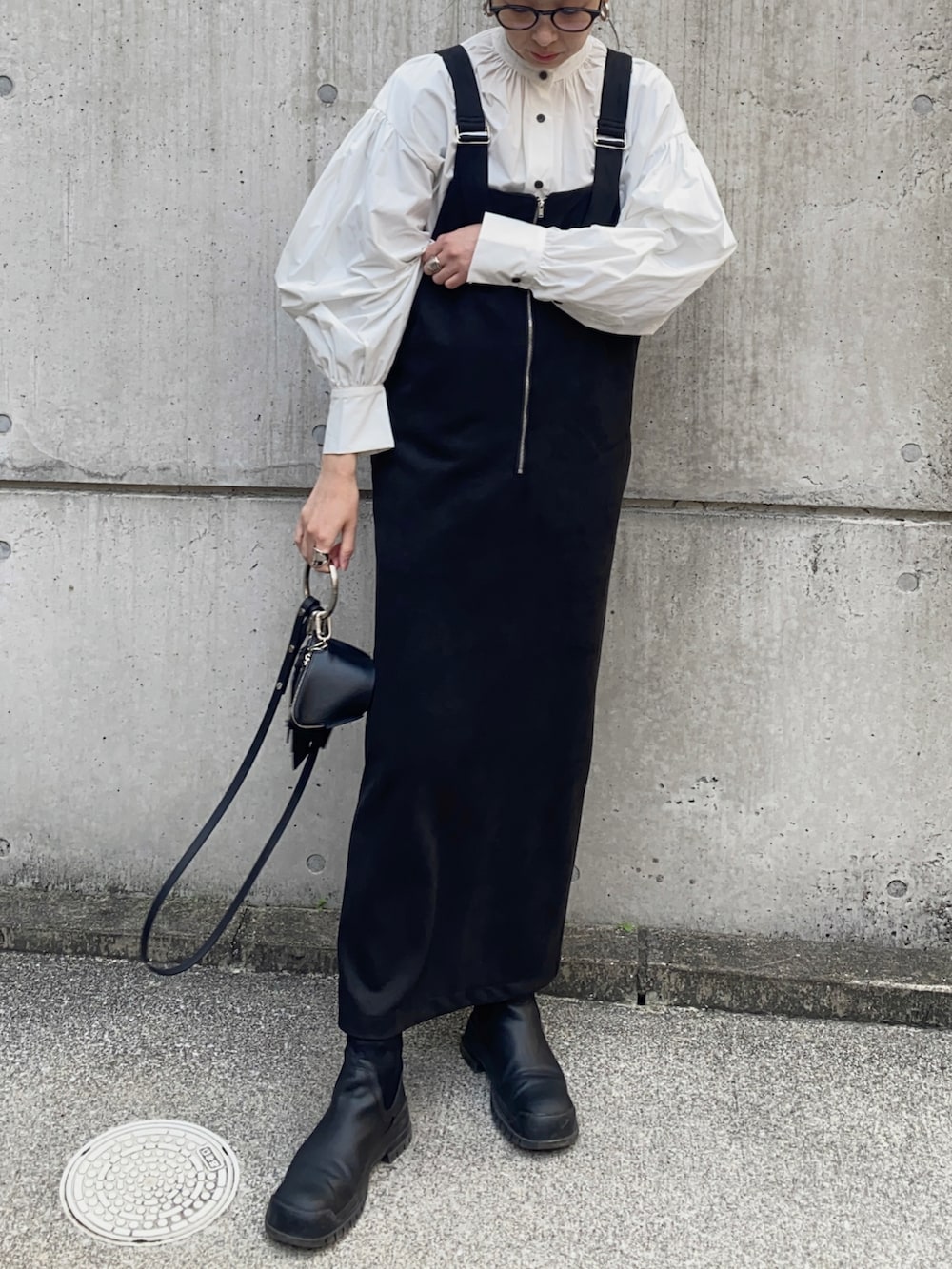 ブラック系のジャンパースカート、ブラック系のショルダーバッグ、ホワイト系のシャツ/ブラウスを着用したレディースの冬コーディネートの2枚目の写真
