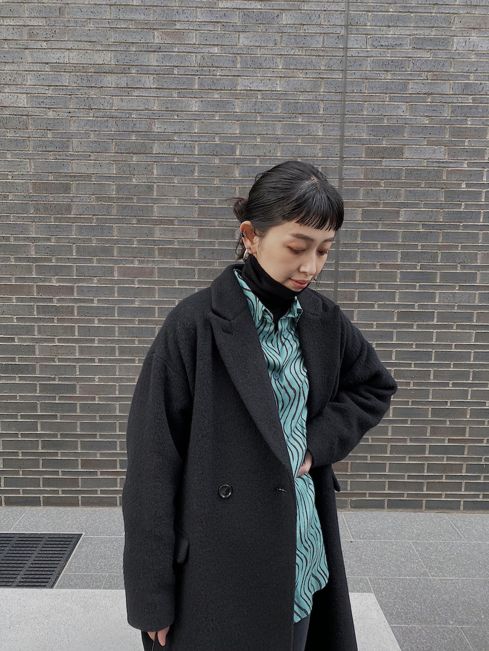 ブルー系のシャツ/ブラウス、ブラック系のニット/セーター、ブラック系のチェスターコートを着用したレディースの冬コーディネートの2枚目の写真