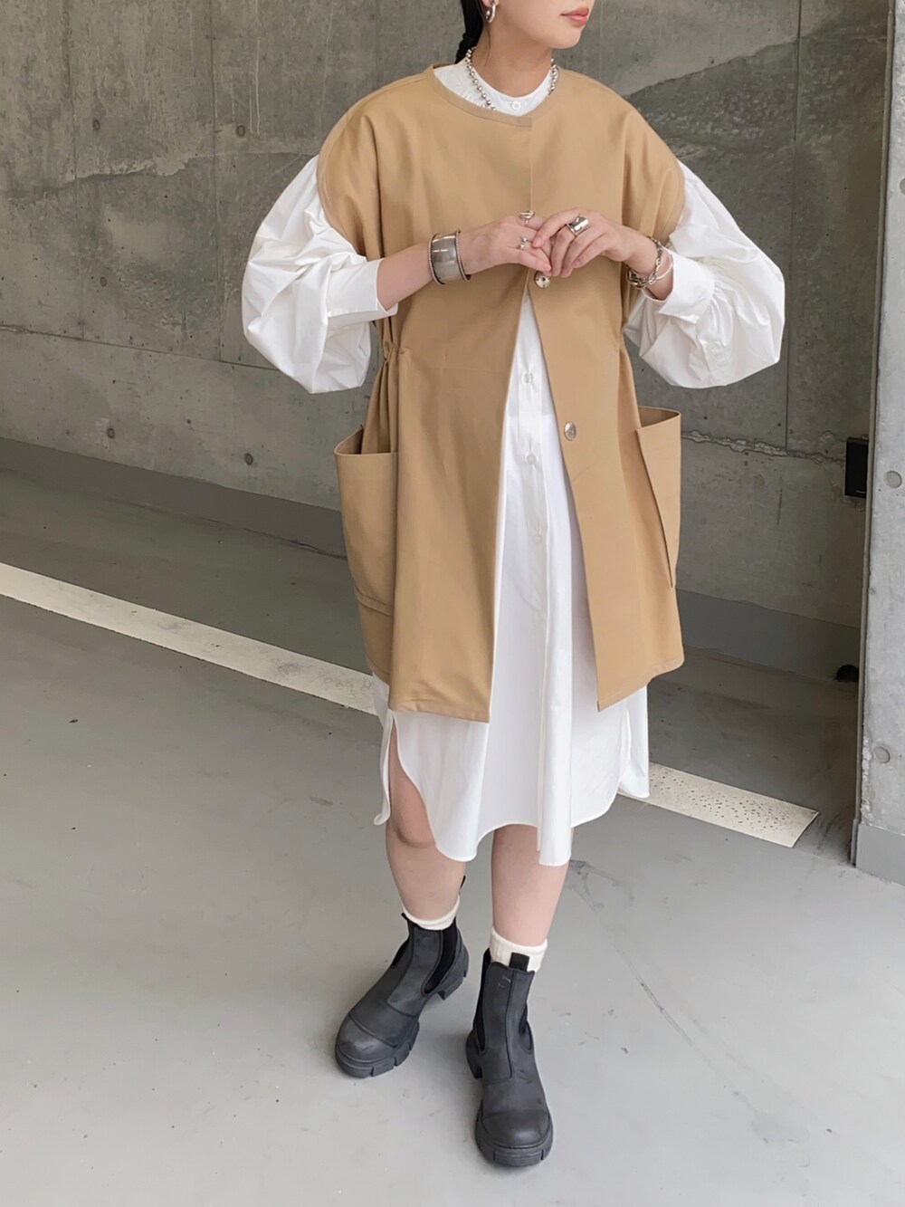 ベージュ系のベスト、ホワイト系のシャツワンピース、ブラック系のブーツを着用したレディースの秋コーディネートの2枚目の写真