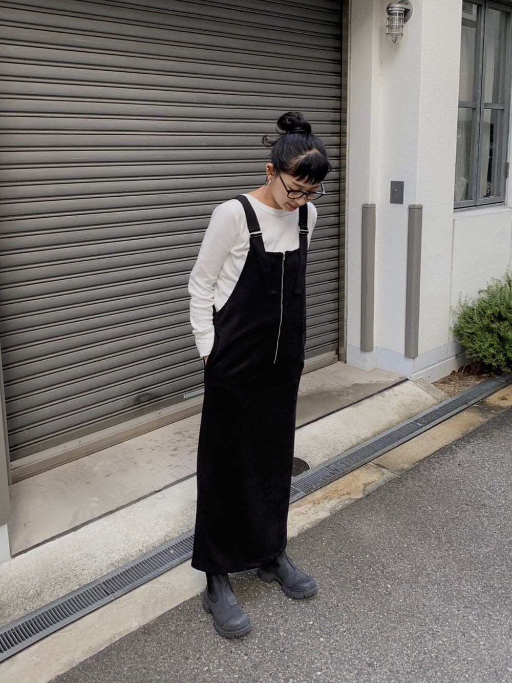 ブラック系のジャンパースカート、ホワイト系のTシャツ/カットソー、ブラック系のブーツを着用したレディースの秋コーディネートの2枚目の写真