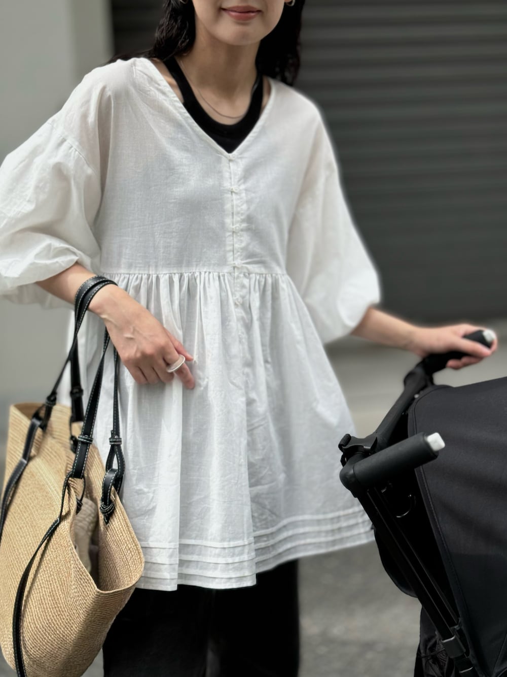 ホワイト系のチュニック、ブラック系のデニムパンツ、ベージュ系のトートバッグを着用したレディースの夏コーディネートの3枚目の写真