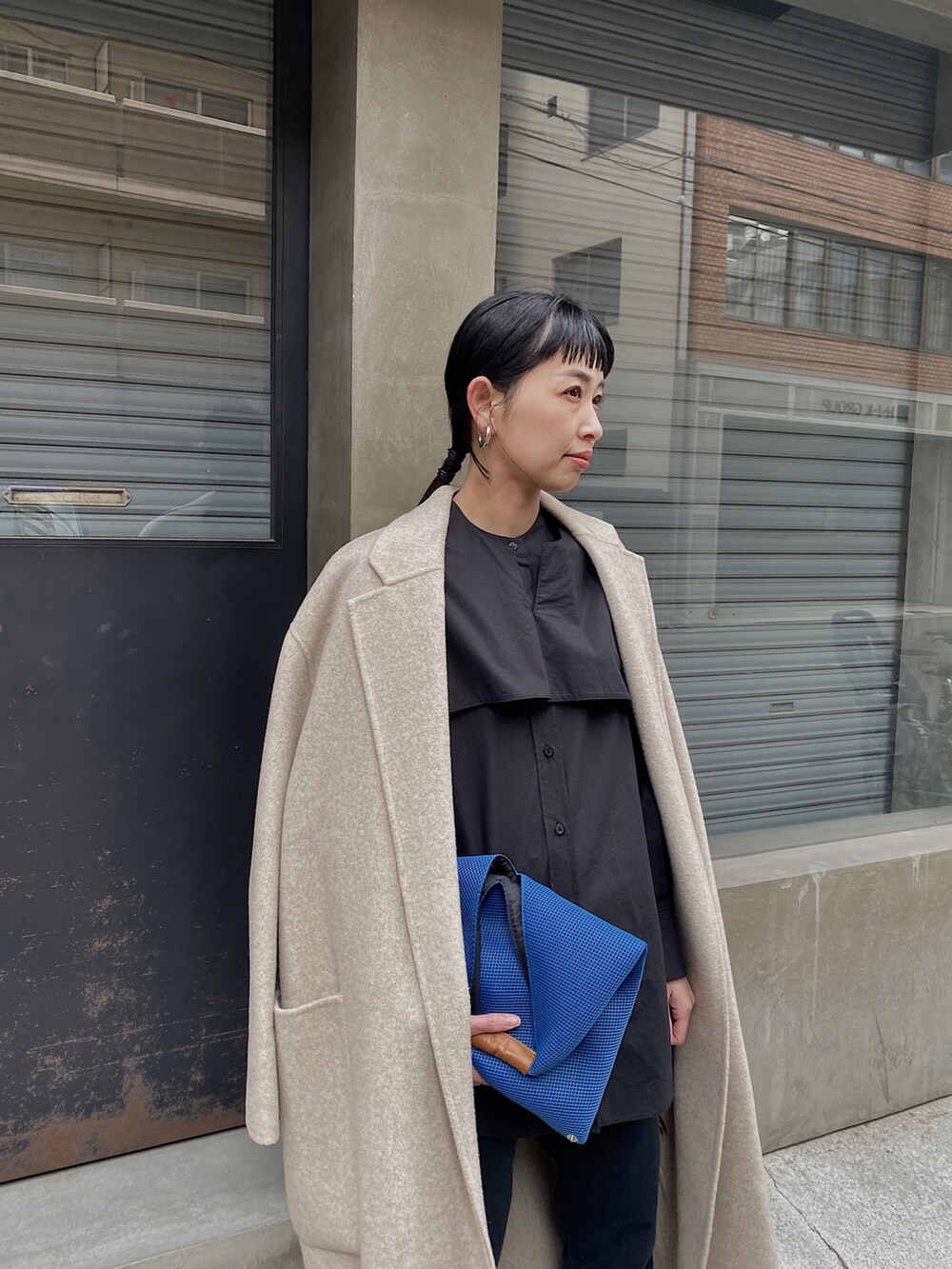 ブラック系のシャツ/ブラウス、ブルー系のハンドバッグ、ホワイト系のチェスターコートを着用したレディースの冬コーディネートの2枚目の写真