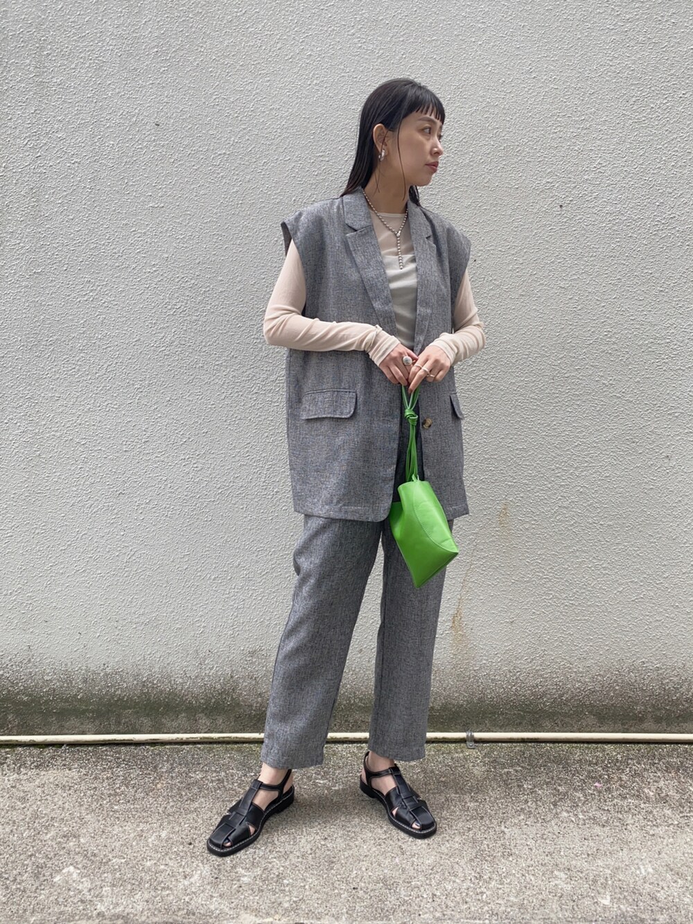 グレー系のベスト、グレー系のスラックス、グリーン系のハンドバッグを着用したレディースの夏コーディネートの2枚目の写真