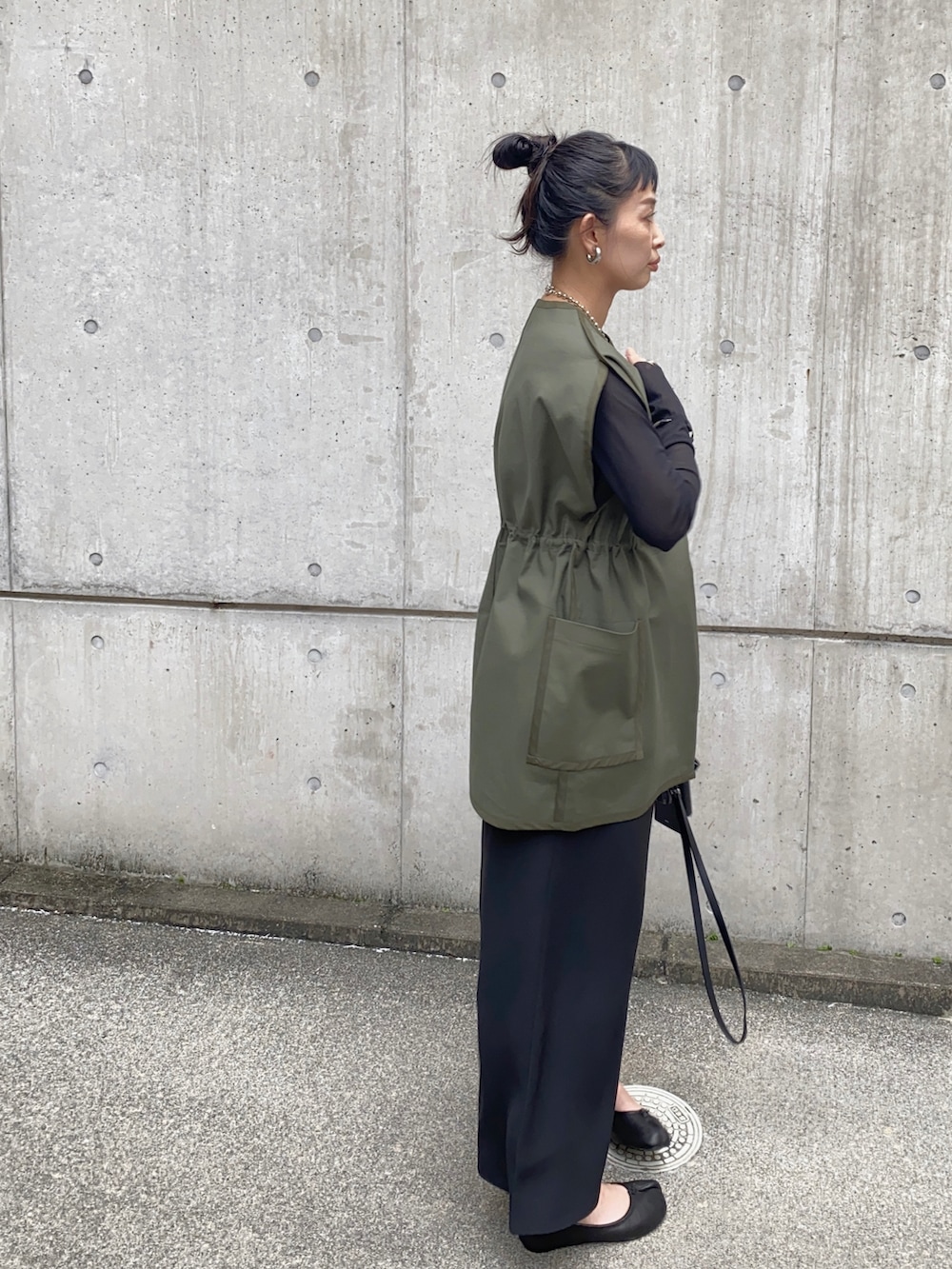 グリーン系のベスト、ブラック系のワンピース、ブラック系のバレエシューズを着用したレディースの秋コーディネートの3枚目の写真