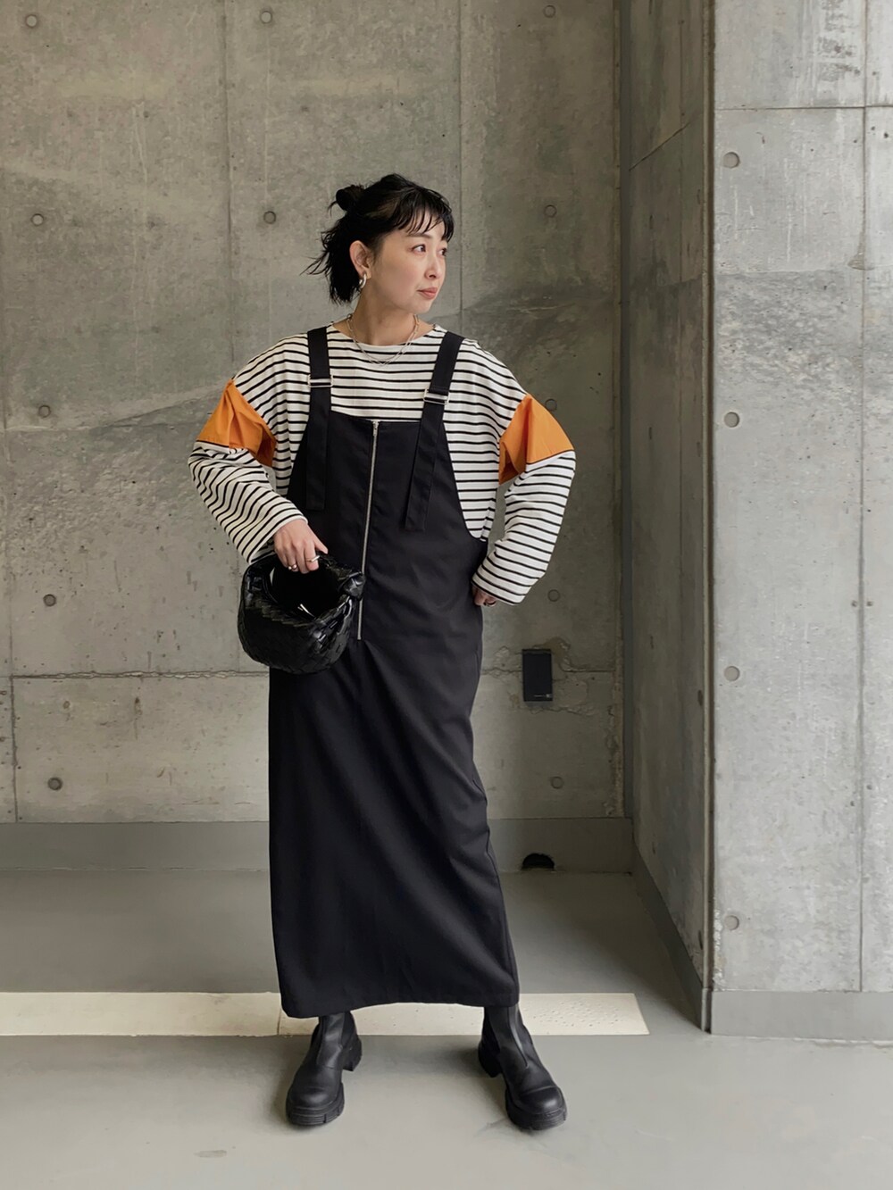 ブラック系のブーツ、オレンジ系のTシャツ/カットソー、ブラック系のジャンパースカートを着用したレディースの春コーディネートの5枚目の写真