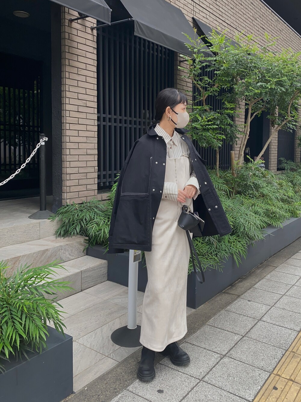 ホワイト系のジャンパースカート、ブラック系のジャケット/アウター、ブラック系のブーツを着用したレディースの秋コーディネートの2枚目の写真