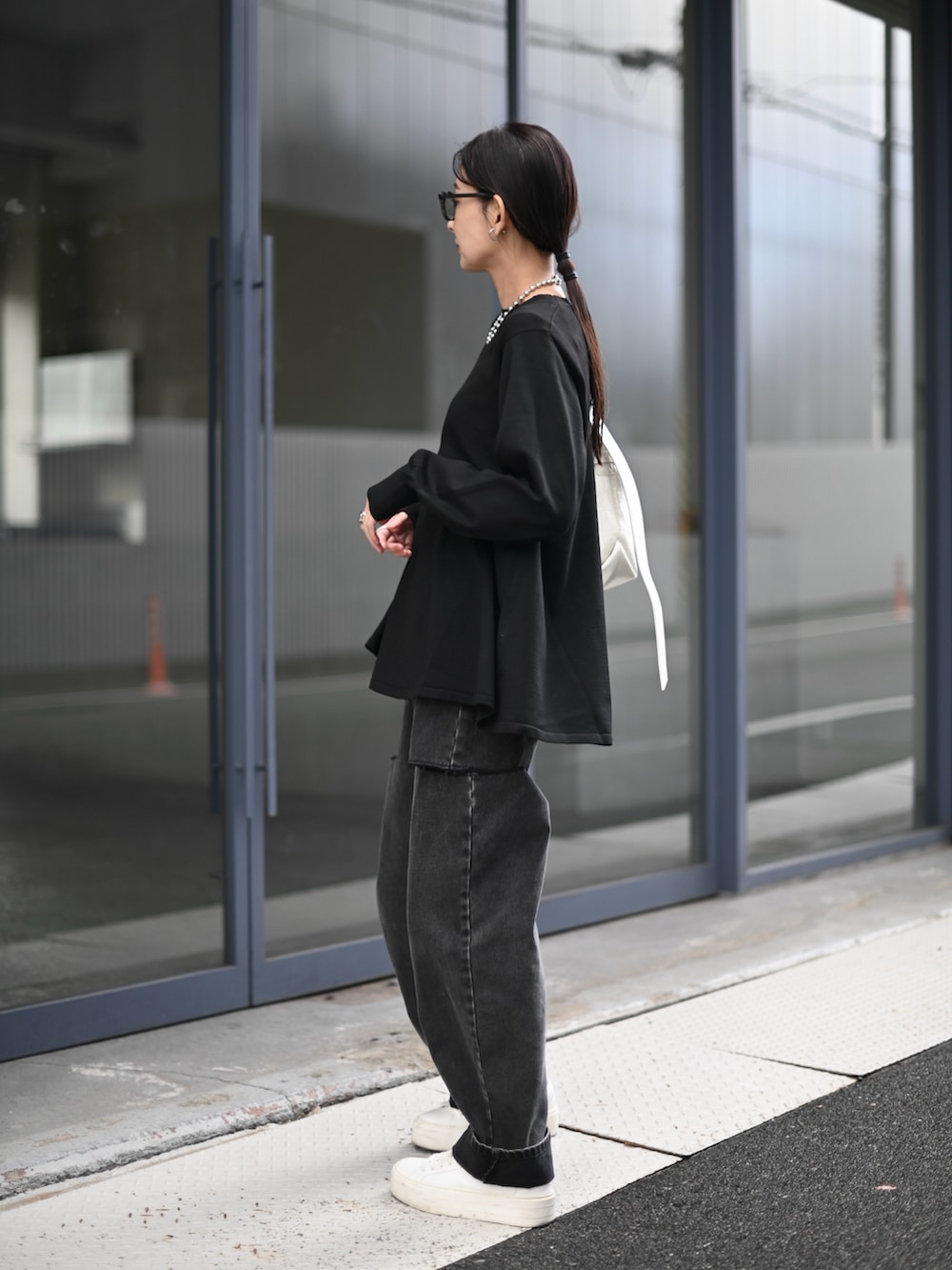 ブラック系のニット/セーター、ブラック系のデニムパンツ、ホワイト系のショルダーバッグを着用したレディースの秋コーディネートの3枚目の写真