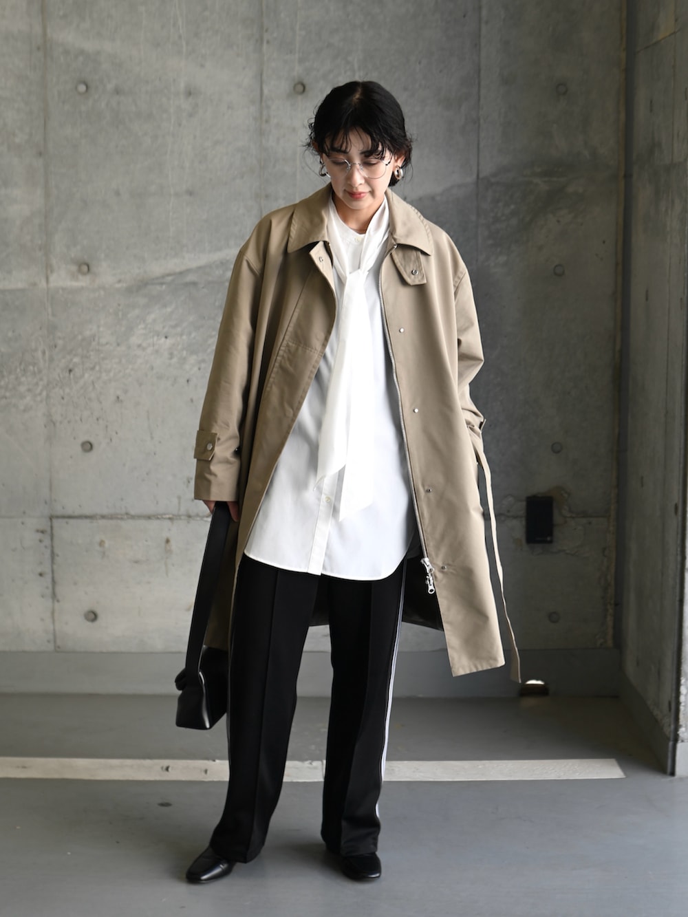 ベージュ系のステンカラーコート、ホワイト系のシャツ/ブラウス、ブラック系のショルダーバッグを着用したレディースの春コーディネートの3枚目の写真