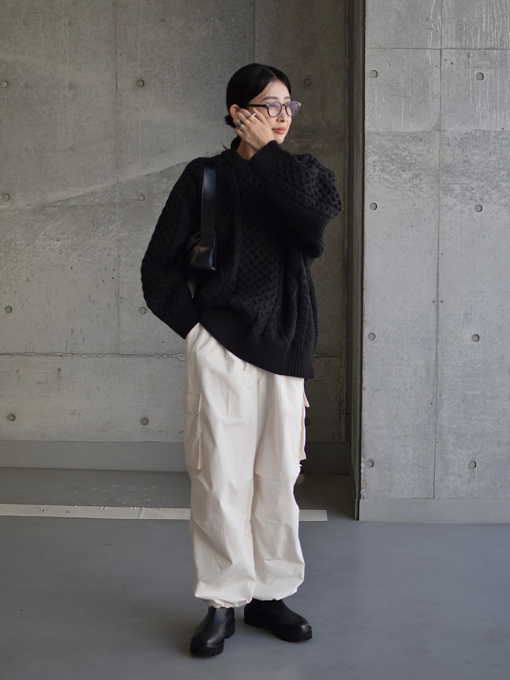 ブラック系のニット/セーター、ブラック系のショルダーバッグ、ブラック系のブーツを着用したレディースの秋コーディネートの2枚目の写真