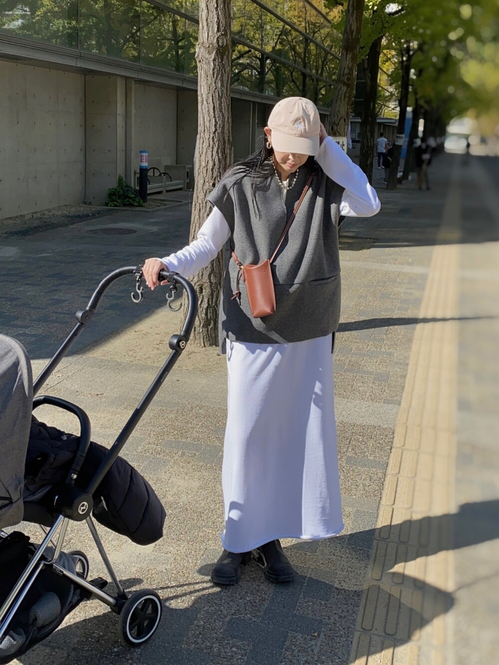 グレー系のベスト、ホワイト系のワンピース、ブラック系のブーツを着用したレディースの秋コーディネートの2枚目の写真