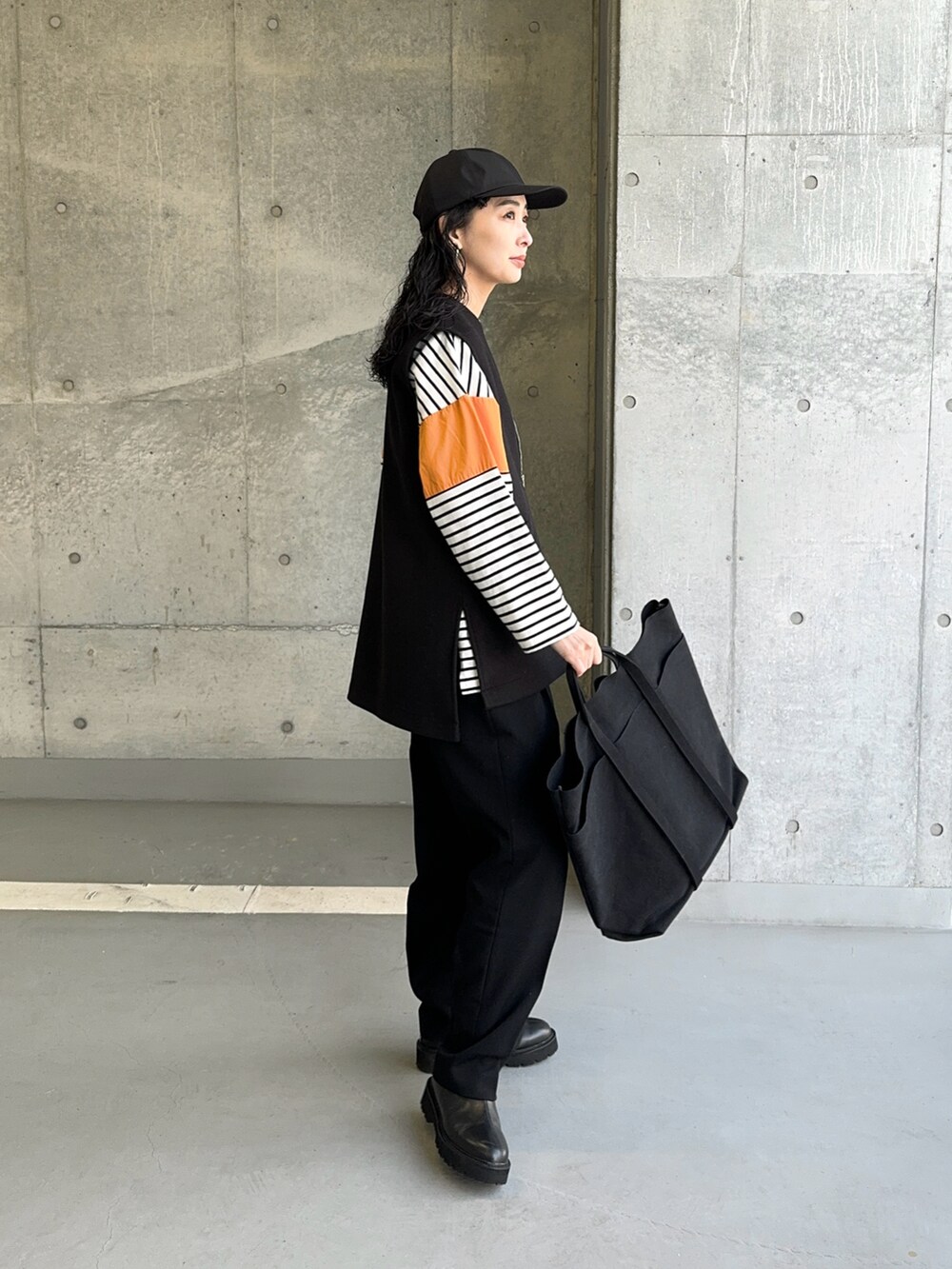 ブラック系のベスト、オレンジ系のTシャツ/カットソー、ブラック系のトートバッグを着用したレディースの冬コーディネートの3枚目の写真