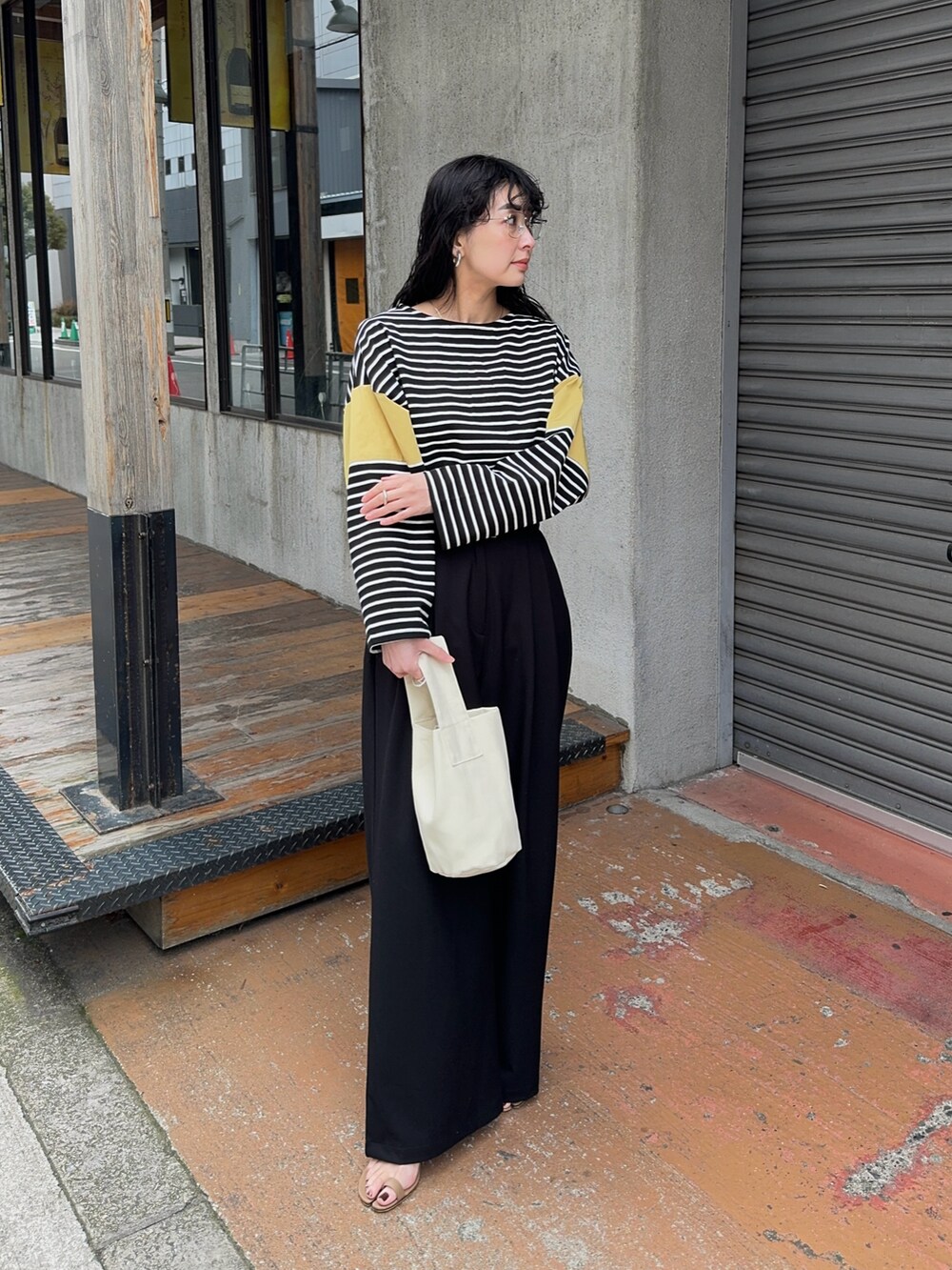 イエロー系のTシャツ/カットソー、ブラック系のスラックス、ブラウン系のサンダルを着用したレディースの春コーディネートの3枚目の写真