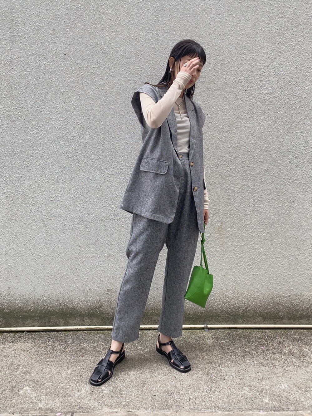 グレー系のベスト、グレー系のスラックス、グリーン系のハンドバッグを着用したレディースの夏コーディネートの3枚目の写真