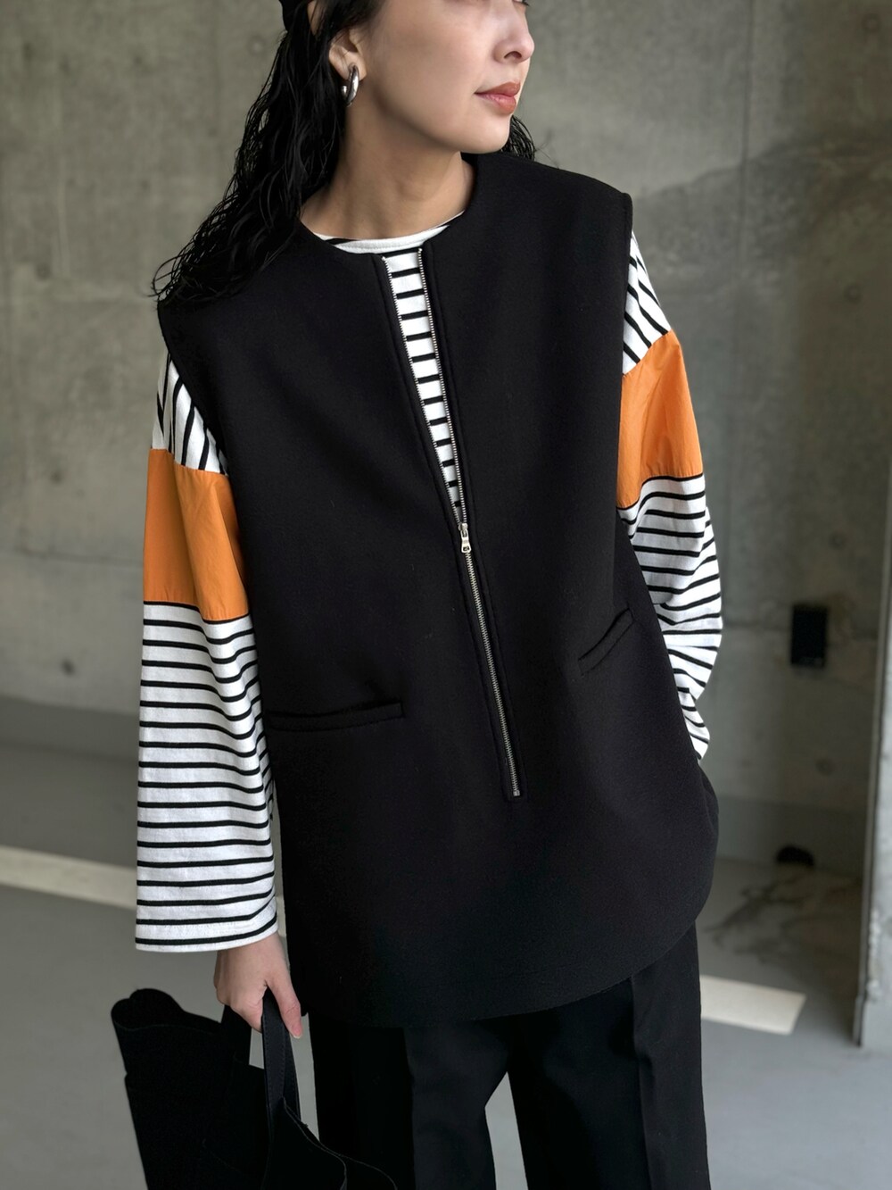 ブラック系のベスト、オレンジ系のTシャツ/カットソー、ブラック系のトートバッグを着用したレディースの冬コーディネートの2枚目の写真