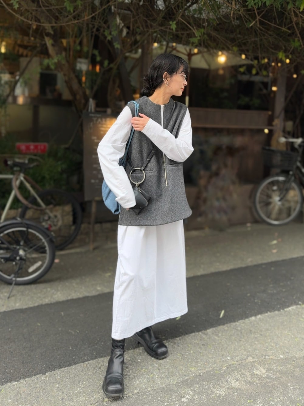 グレー系のベスト、ブラック系のショルダーバッグ、ブラック系のブーツを着用したレディースの秋コーディネートの2枚目の写真