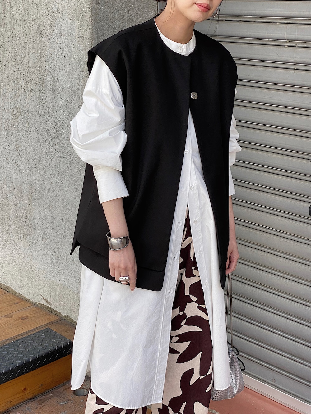 ブラック系のベスト、ホワイト系のシャツワンピース、ブラック系のバレエシューズを着用したレディースの春コーディネートの2枚目の写真