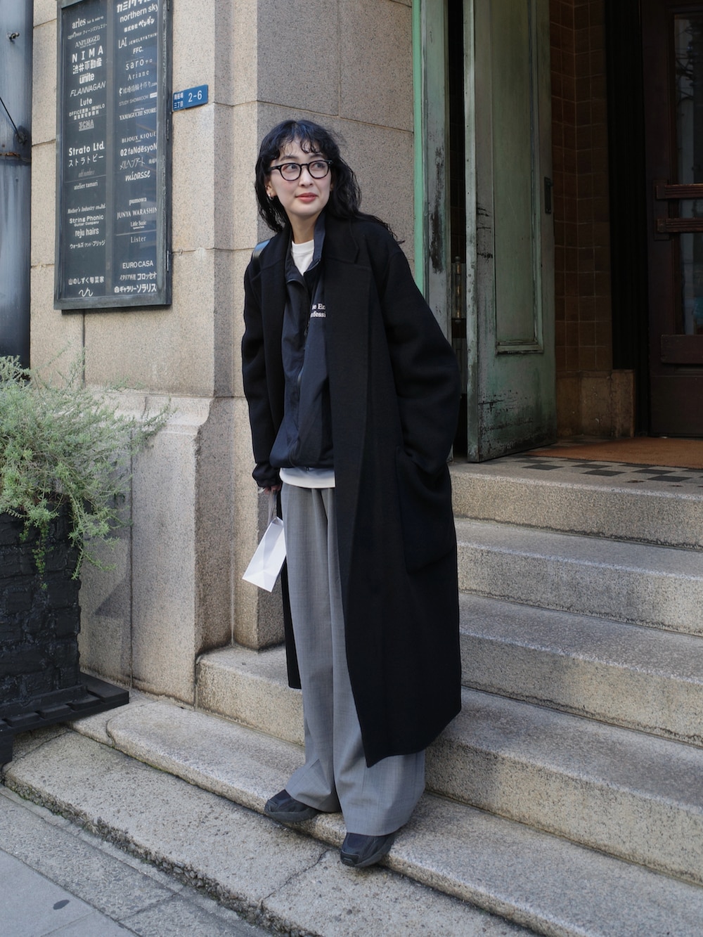 ブラック系のチェスターコート、ブラック系のナイロンジャケット、グレー系のスラックスを着用したレディースの冬コーディネートの4枚目の写真