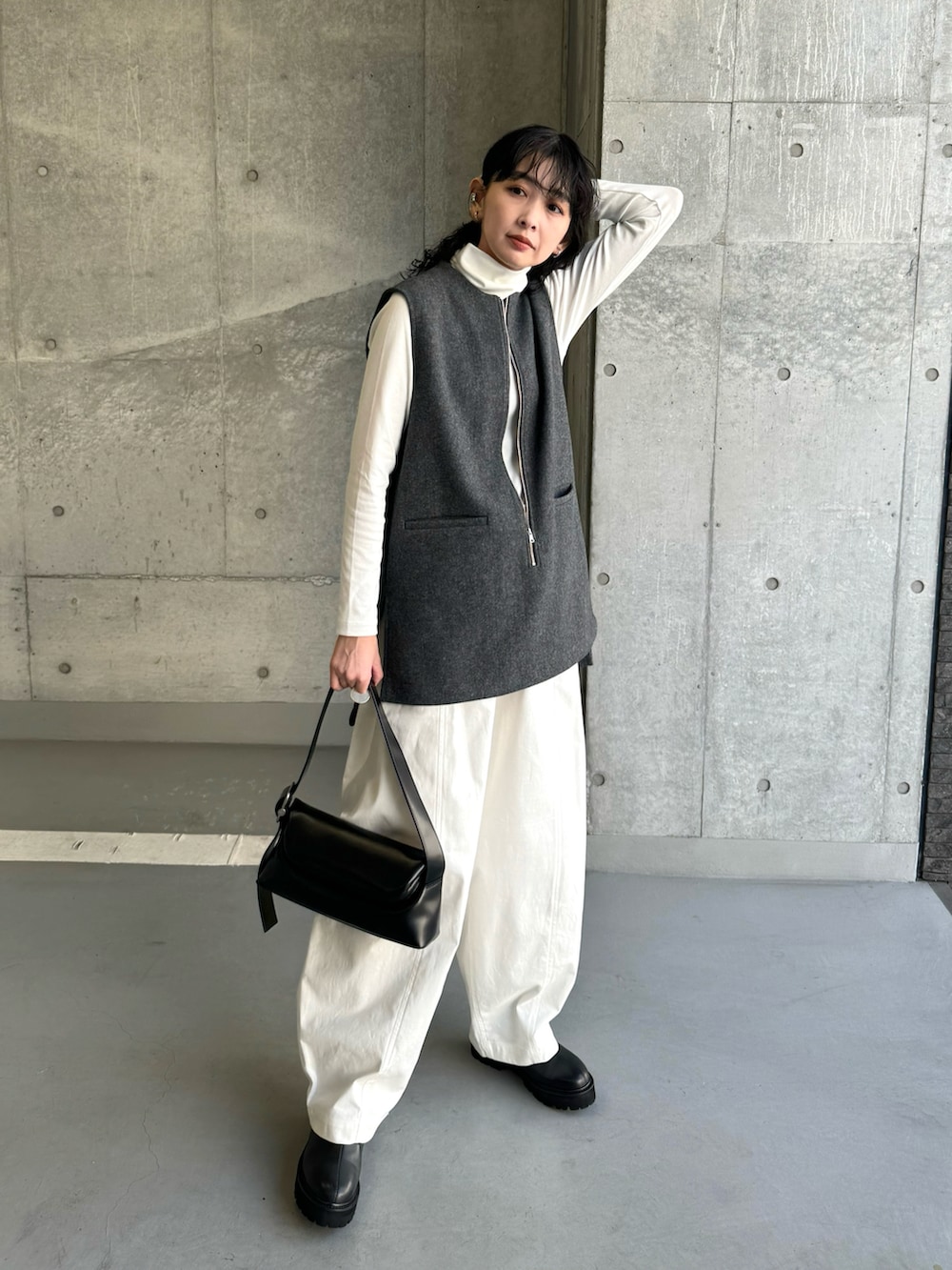 グレー系のベスト、ホワイト系のチノパンツ、ブラック系のブーツを着用したレディースの冬コーディネートの2枚目の写真