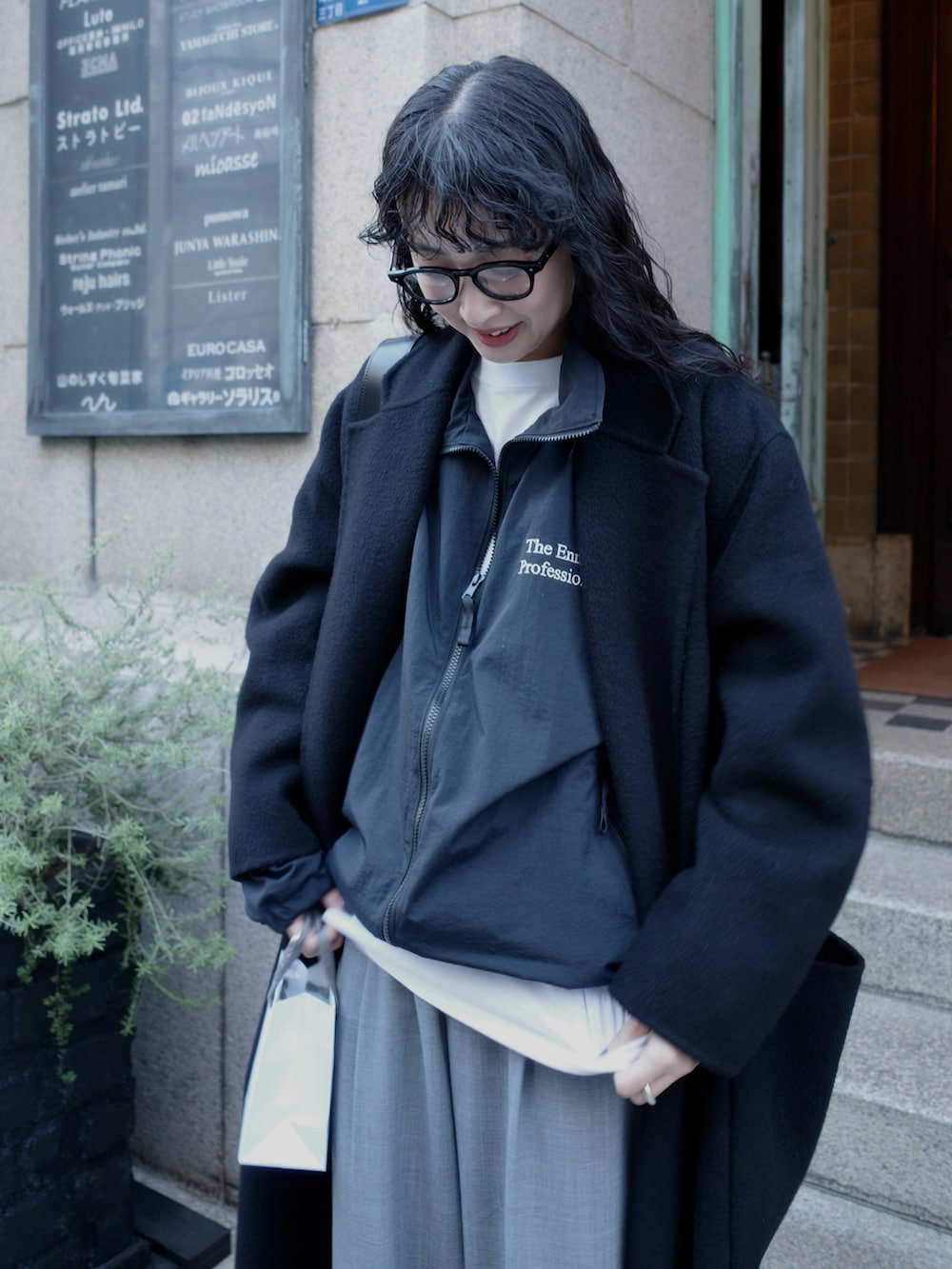 ブラック系のチェスターコート、ブラック系のナイロンジャケット、グレー系のスラックスを着用したレディースの冬コーディネートの3枚目の写真