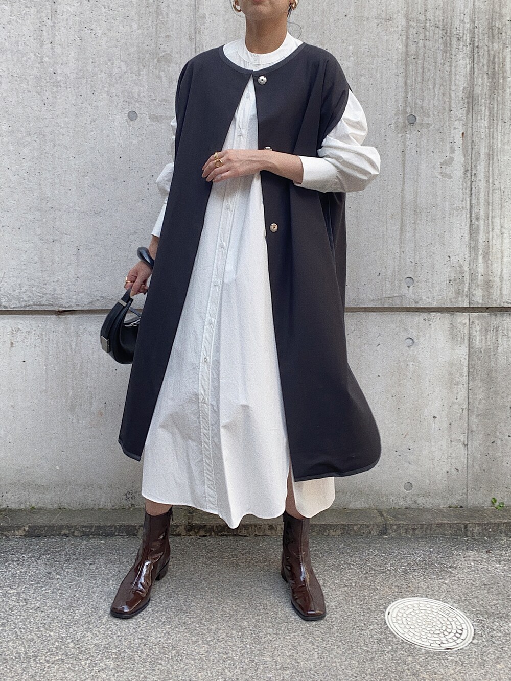 ブラック系のその他アウター、ホワイト系のシャツワンピース、ブラウン系のブーツを着用したレディースの秋コーディネートの2枚目の写真