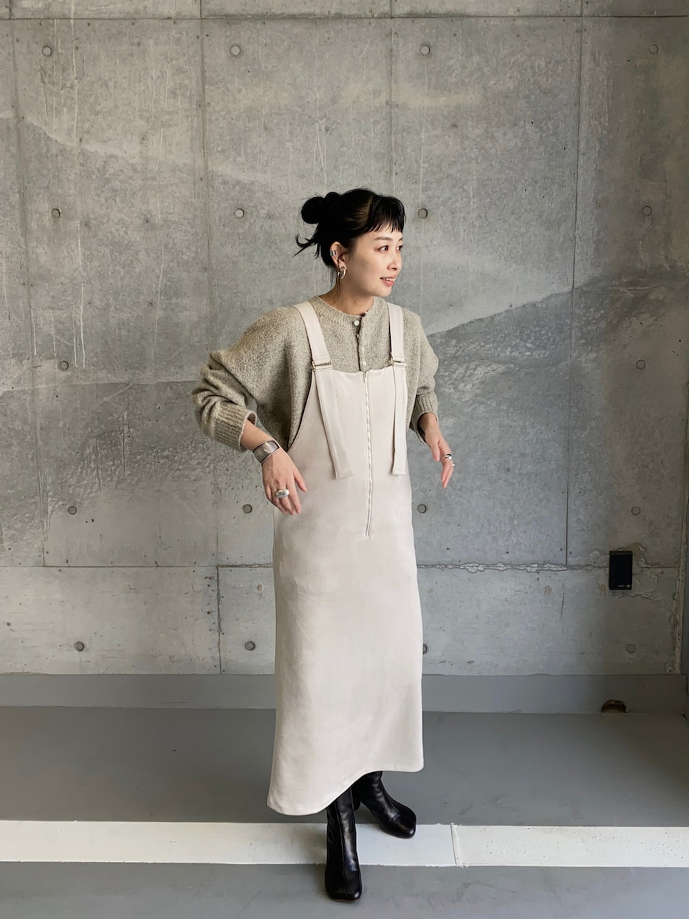 ホワイト系のジャンパースカート、グレー系のニット/セーター、ブラック系のブーツを着用したレディースの秋コーディネートの4枚目の写真