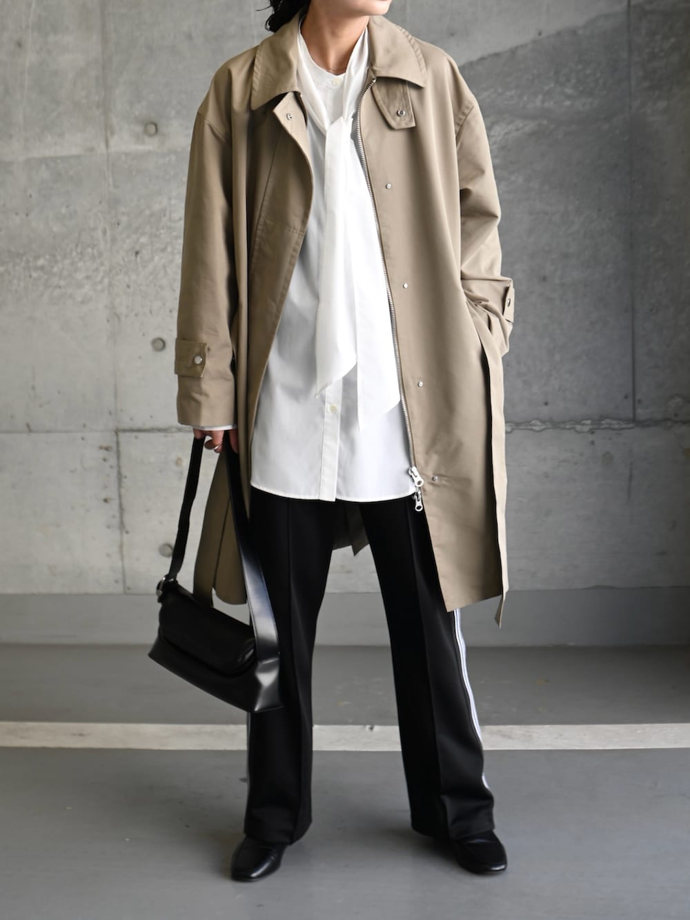 ベージュ系のステンカラーコート、ホワイト系のシャツ/ブラウス、ブラック系のショルダーバッグを着用したレディースの春コーディネートの2枚目の写真