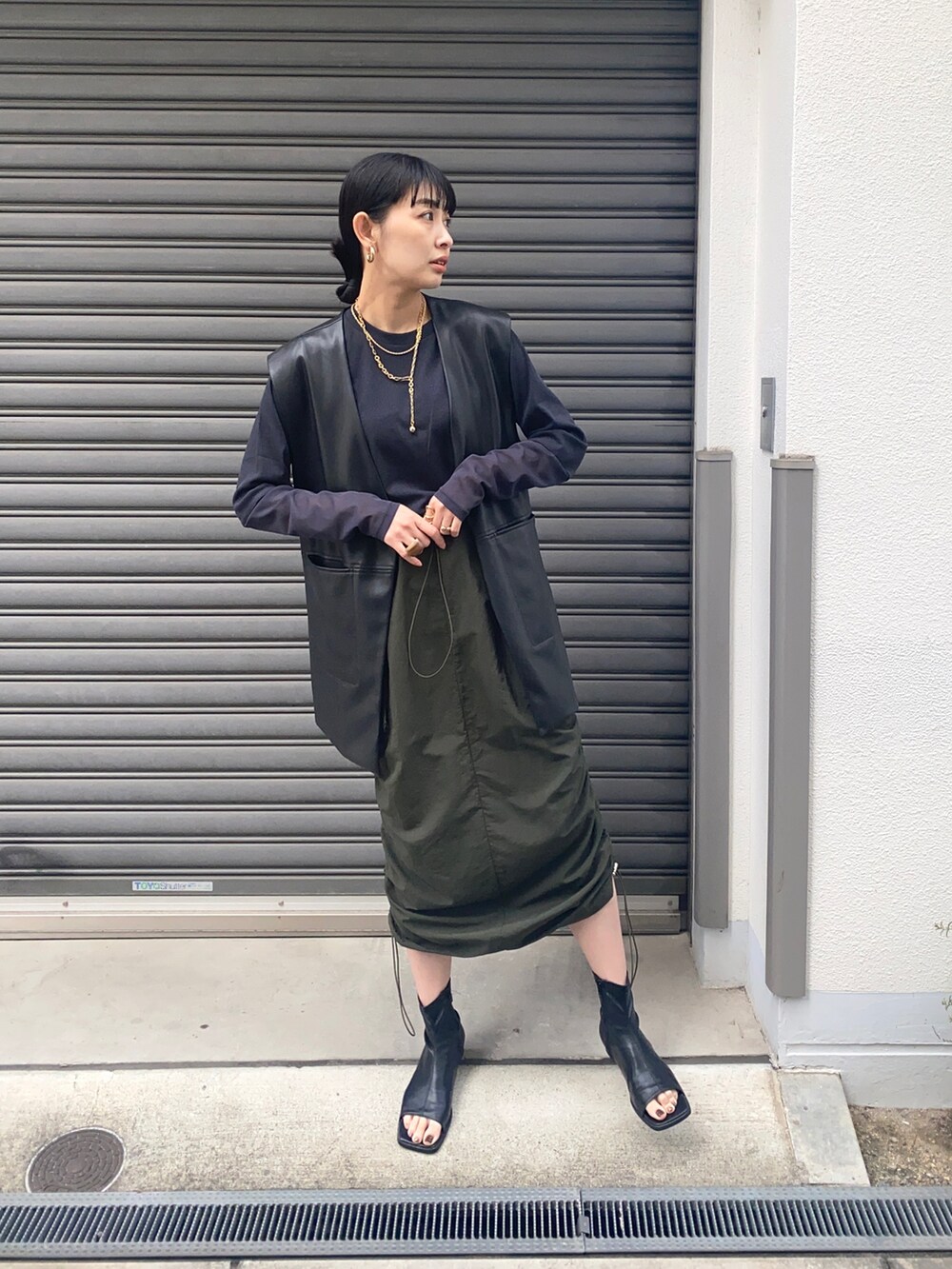 ブラック系のベスト、グリーン系のスカート、ブラック系のTシャツ/カットソーを着用したレディースの春コーディネートの2枚目の写真