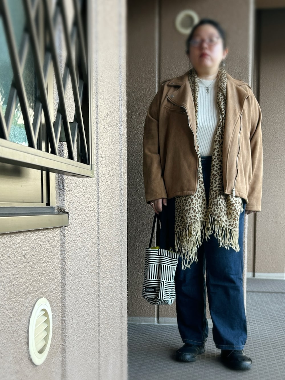 ブラウン系のライダースジャケット、ベージュ系のニット/セーター、ブルー系のデニムパンツを着用したレディースの冬コーディネートの2枚目の写真