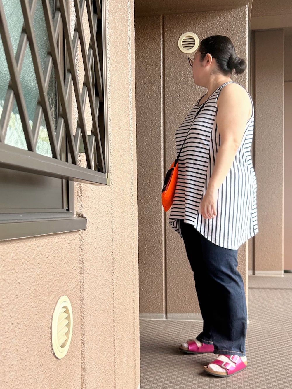 ホワイト系のタンクトップ、オレンジ系のショルダーバッグ、ブルー系のデニムパンツを着用したレディースの夏コーディネートの2枚目の写真