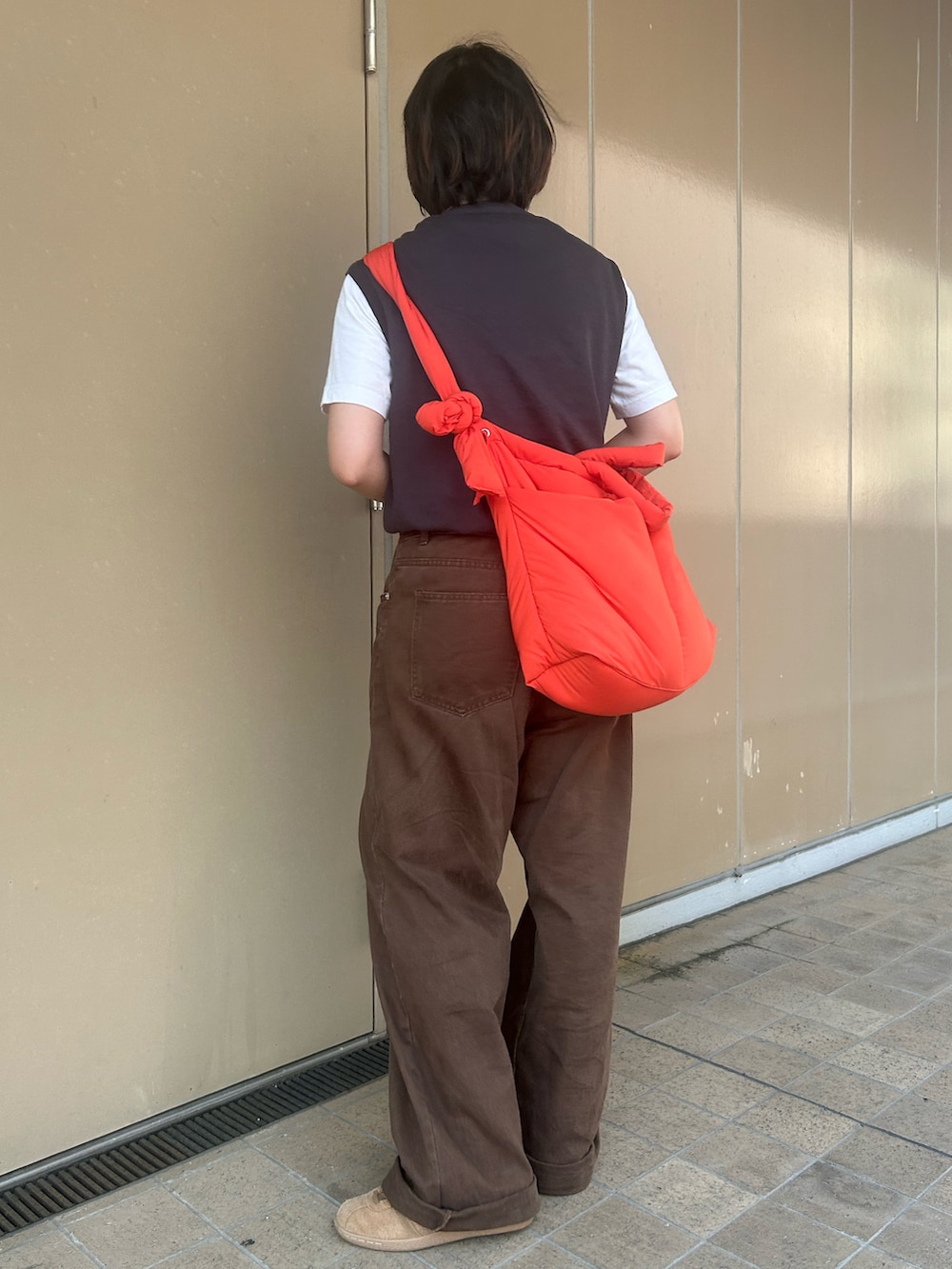 オレンジ系のトートバッグ、ブラウン系のスニーカー、ホワイト系のTシャツ/カットソーを着用したレディースの夏コーディネートの2枚目の写真
