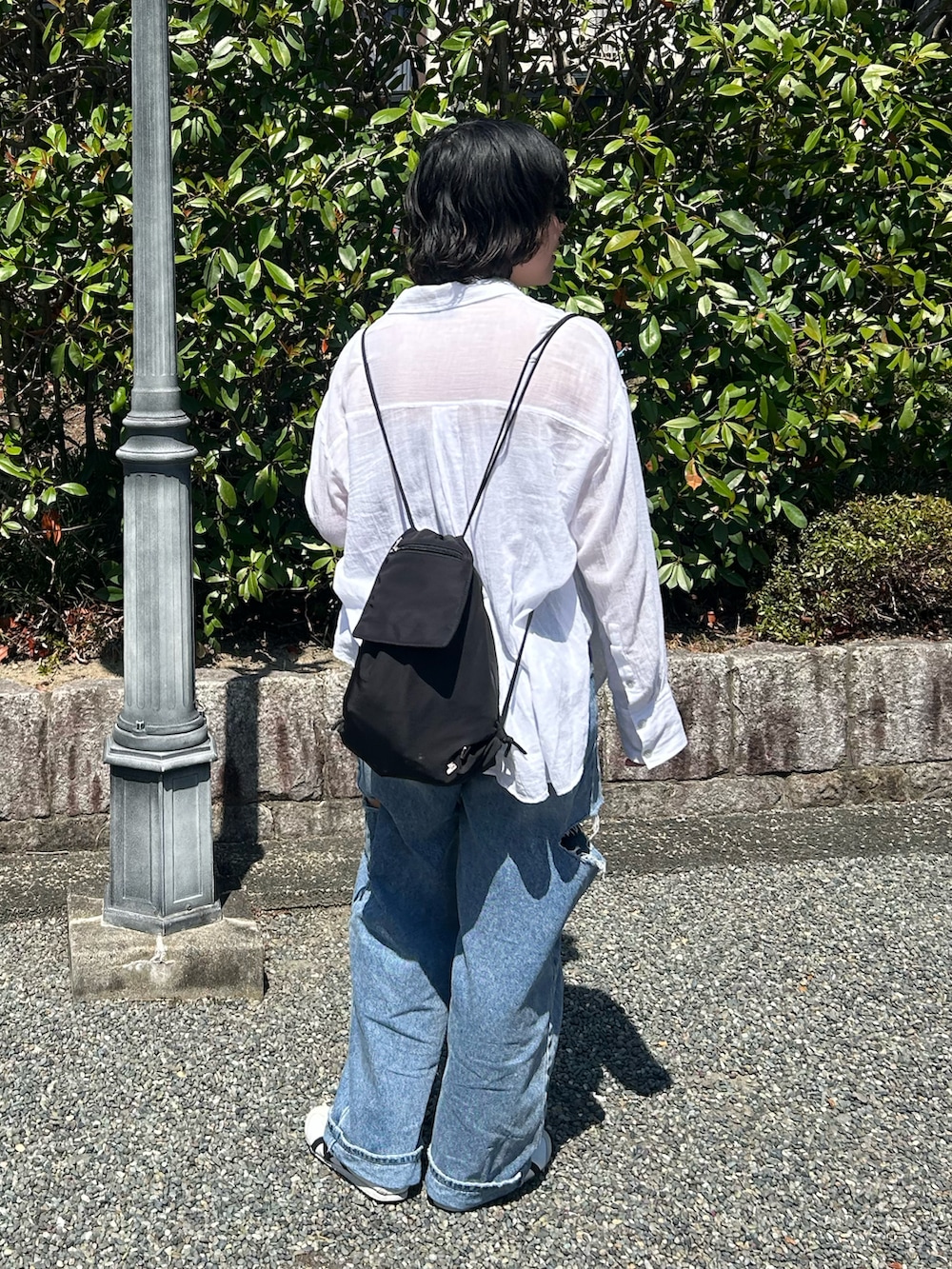 ブルー系のデニムパンツ、ブラック系のバックパック/リュック、ホワイト系のスニーカーを着用したレディースの夏コーディネートの2枚目の写真