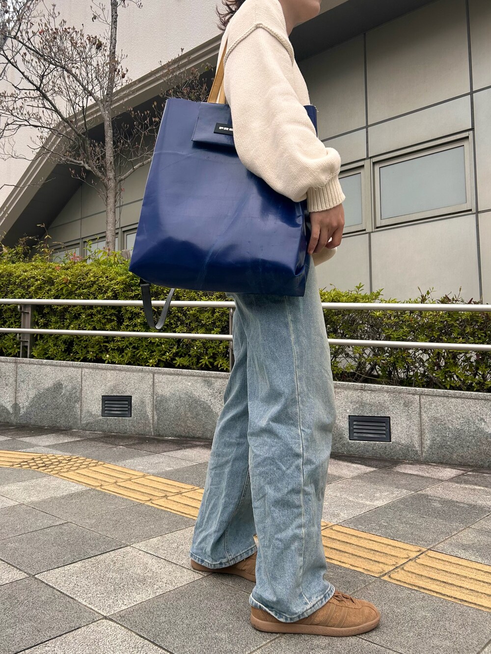 ブラウン系のスニーカー、ホワイト系のニット/セーター、ブルー系のデニムパンツを着用したレディースの春コーディネートの4枚目の写真
