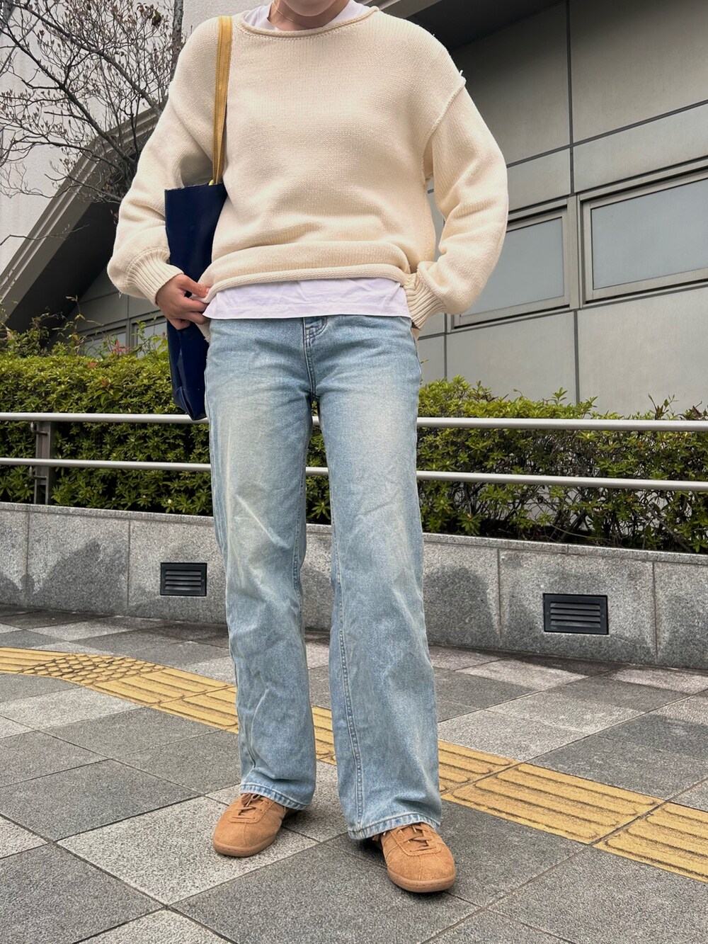 ブラウン系のスニーカー、ホワイト系のニット/セーター、ブルー系のデニムパンツを着用したレディースの春コーディネートの2枚目の写真