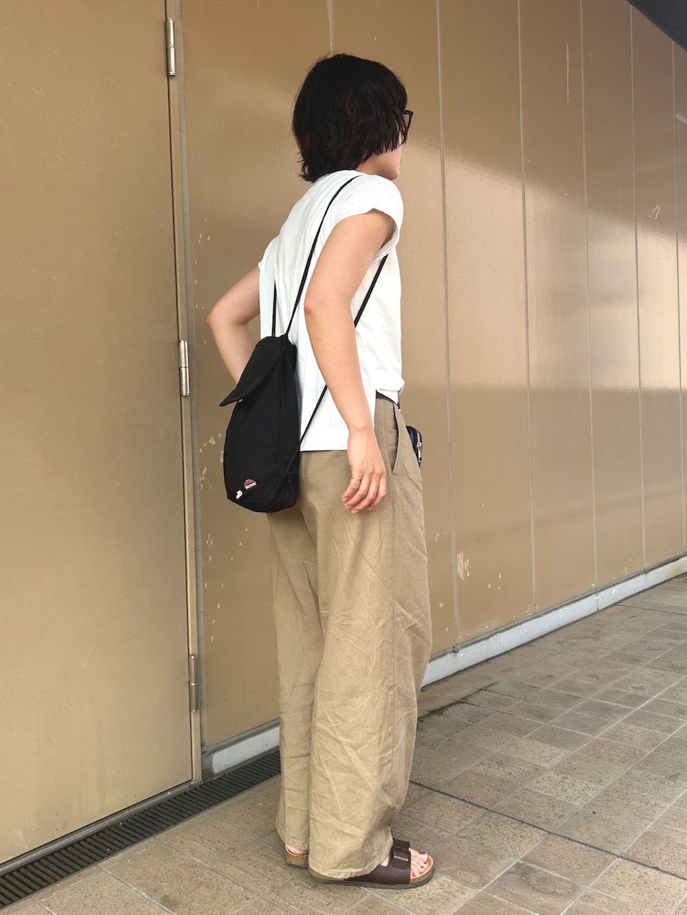 ブラック系のバックパック/リュック、ホワイト系のTシャツ/カットソー、ブラウン系のサンダルを着用したレディースの夏コーディネートの2枚目の写真