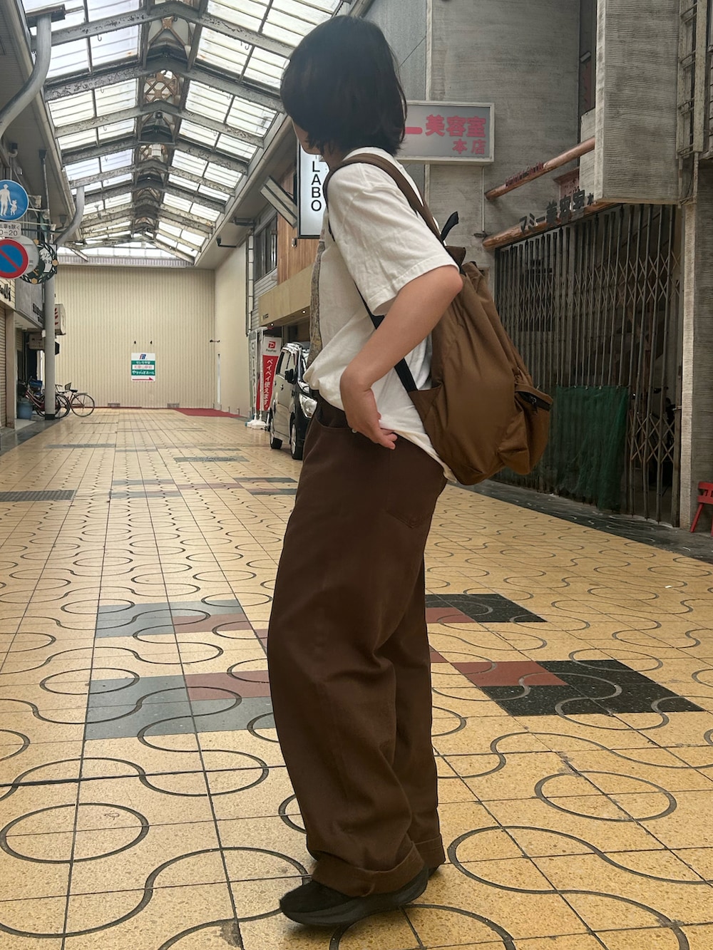 ブラック系のスニーカー、ホワイト系のTシャツ/カットソー、ブラウン系のデニムパンツを着用したレディースの夏コーディネートの2枚目の写真