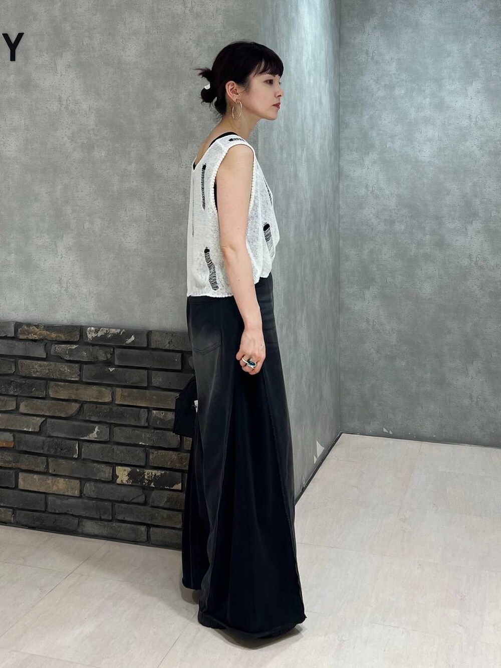 ブラック系のデニムパンツ、ブラック系のショルダーバッグ、ホワイト系のベストを着用したレディースの夏コーディネートの3枚目の写真