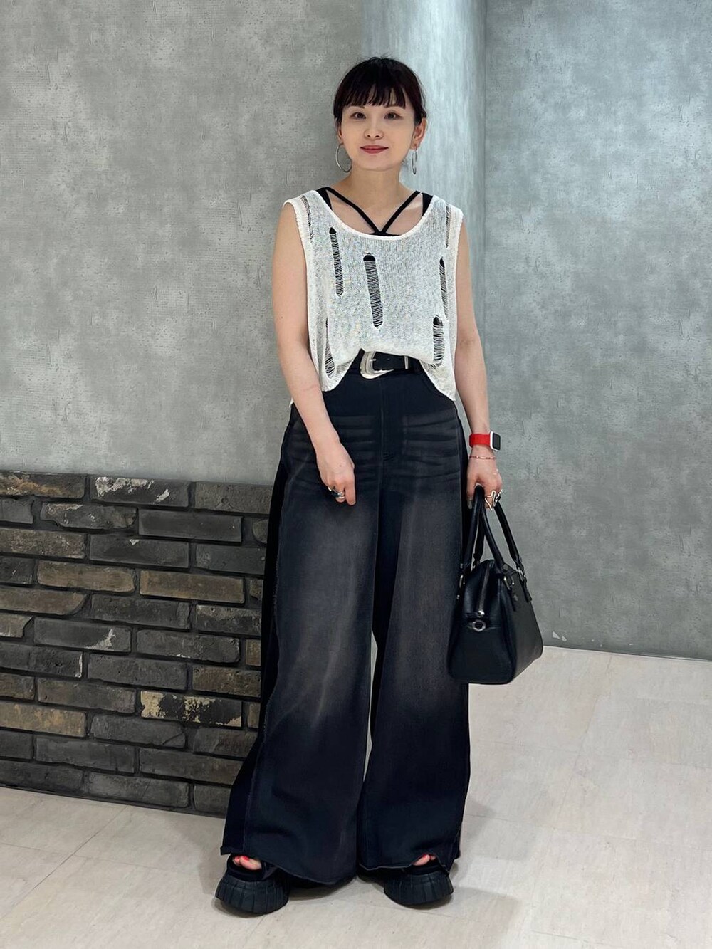 ブラック系のデニムパンツ、ブラック系のショルダーバッグ、ホワイト系のベストを着用したレディースの夏コーディネートの2枚目の写真