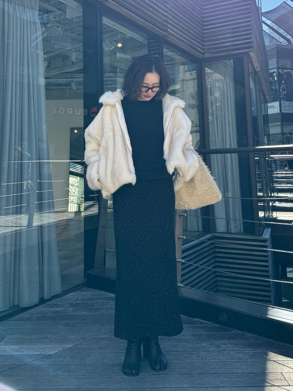 ホワイト系のブルゾン、ベージュ系のトートバッグ、ブラック系のスカートを着用したレディースの冬コーディネートの2枚目の写真